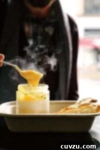 Person with a spoon digging into a glass jar of coddle eggs with potato puree underneath, slice of bread nearby
