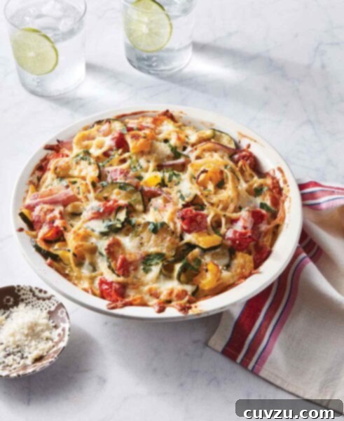 Spaghetti primavera pie in a large dish—spaghetti topped with zucchini, tomatoes, onions, Parmesan and mozzarella cheese.
