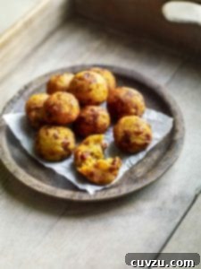 A wooden bowl filled with golf-ball-size fried potato and chouriço balls on a wooden tray.