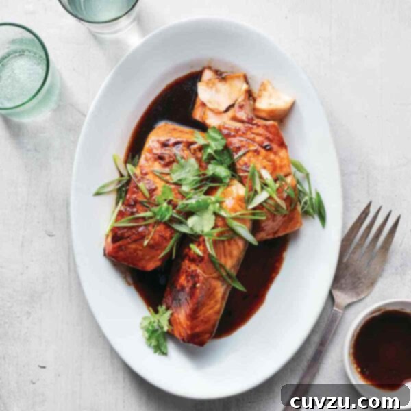 Three salmon filets on an oval platter in a soy caramel sauce, topped with cilantro and scallions.