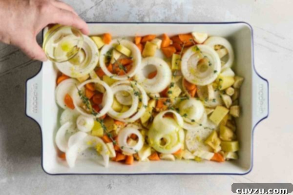 A person drizzling oil over a tray of root vegetables and onion slices.