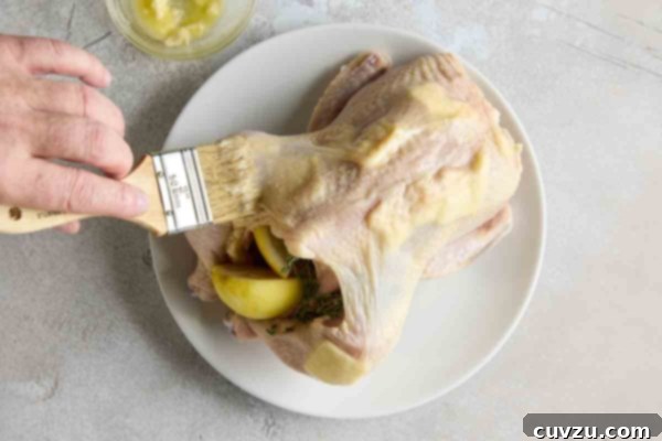 A person brushing a stuffed chicken with melted butter.