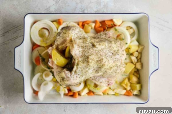 A stuffed chicken on a bed of root vegetables and onion slices.