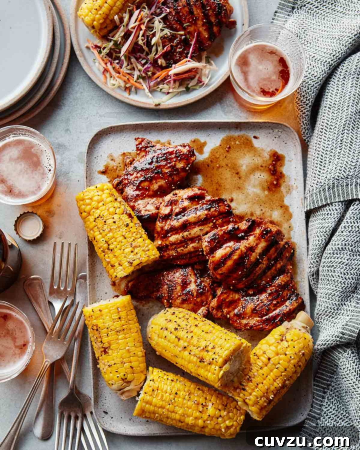 Sticky Balsamic BBQ Chicken Thighs 2 A tray of chicken thighs with balsamic barbecue sauce, corn on the cob, glasses of beer, forks, and plates, ready to be served