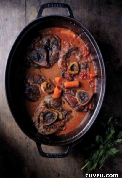 Tender Braised Veal Osso Bucco 3 Five veal osso bucco, with carrots, and tomato sauce in a black cast-iron pot.