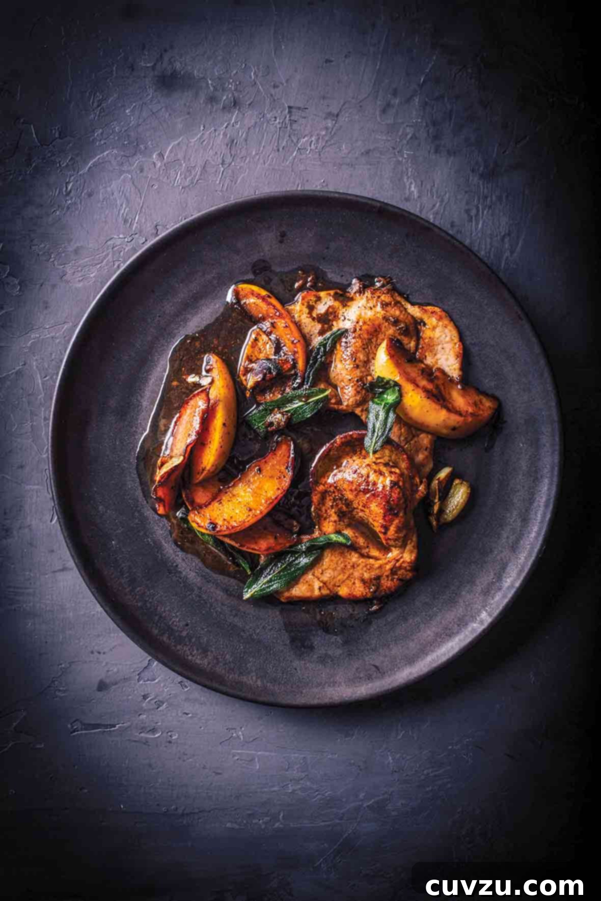 Golden Pork Scallopini with Apples and Fragrant Sage 2 A dark purple plate with pork scallopini with apples and sage in a sauce