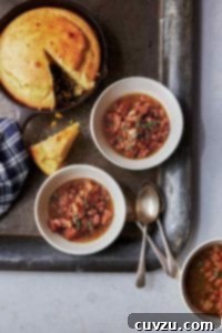 Three white bowls of pork and pinto beans chili on a metal tray with cornbread in a skillet