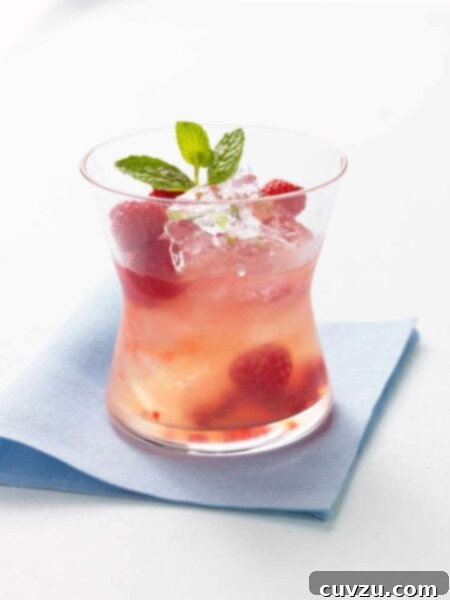 A glass of raspberry lemonade with tequila garnished with a mint sprig.