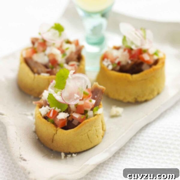 Three Mexican sopes on a rustic platter with a glass of white wine in the background.