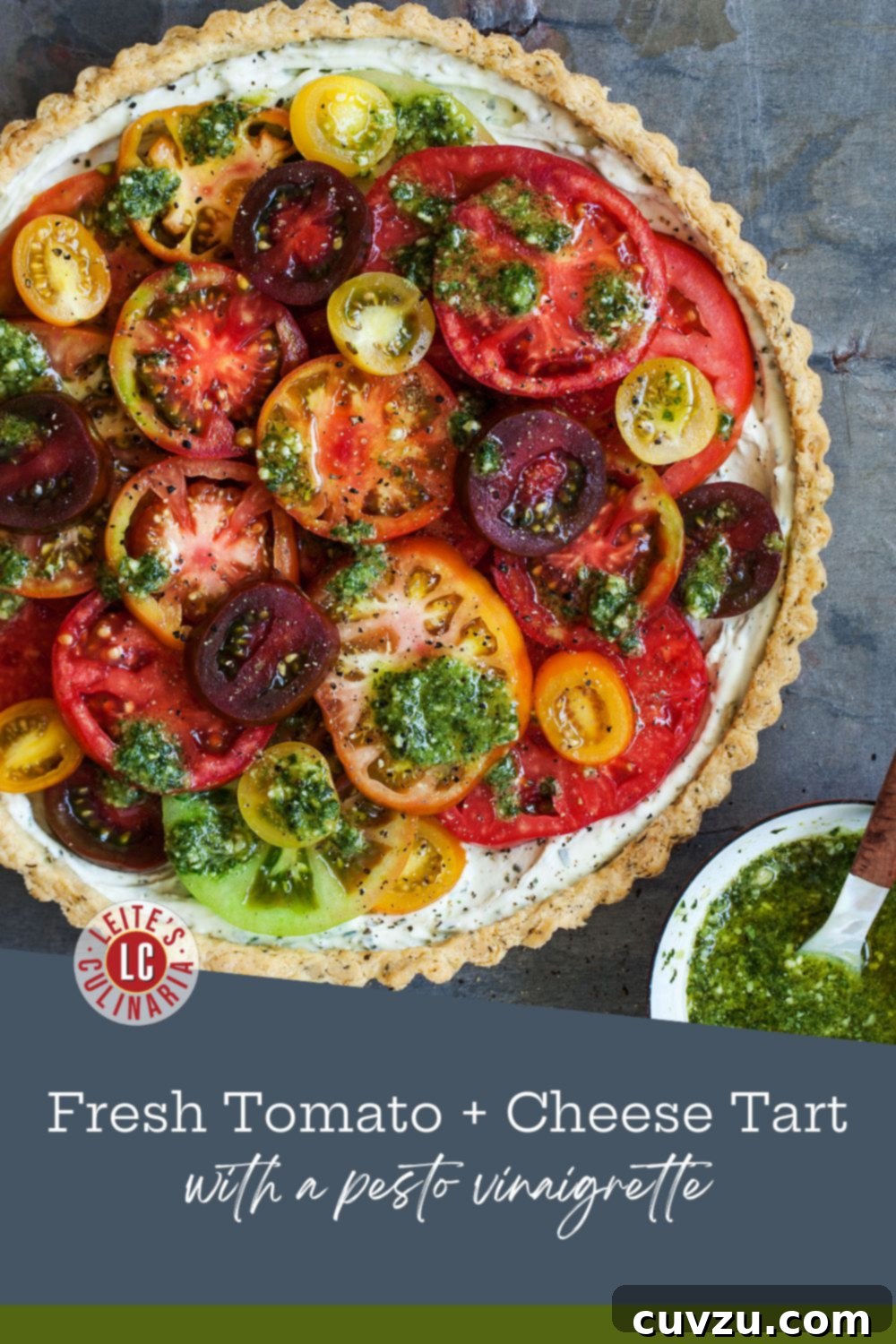 Savory Garden Tomato Galette 3 A vibrant, multi-colored heirloom tomato tart displayed on a dark slate background, accompanied by a small white bowl of bright green pesto vinaigrette.