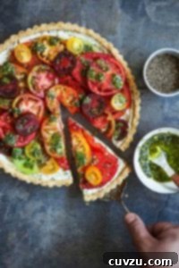 A person removing a slice of fresh tomato tart with a lifter and a bowl of pesto and black pepper on the side.