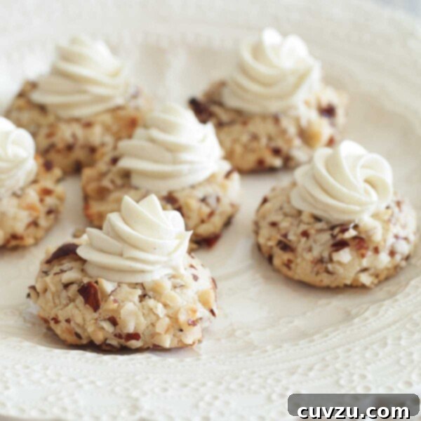 A stack of scalloped white plates with six thumbprint cookies on top, each garnished with white chocolate ganache.