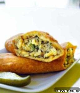 A potato piroshki cut in half, revealing the filling, on a plate with a pickle wedge
