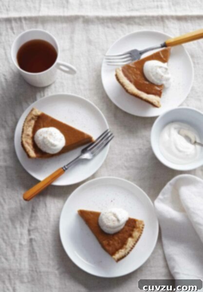 Maple pumpkin pie slices on 3 plates, topped with whipping cream. Flanked by a napkin, a cup of coffee, and a bowl of whipping cream.