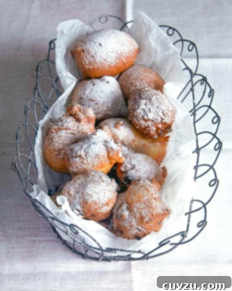 Oliebollen, or Dutch doughnuts, in a wire basket, covered with powdered sugar on a white tablecloth.