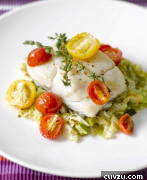A delicious piece of oven-roasted halibut with cherry tomatoes and thyme on a bed of cooked cabbage, illustrating the recipe.