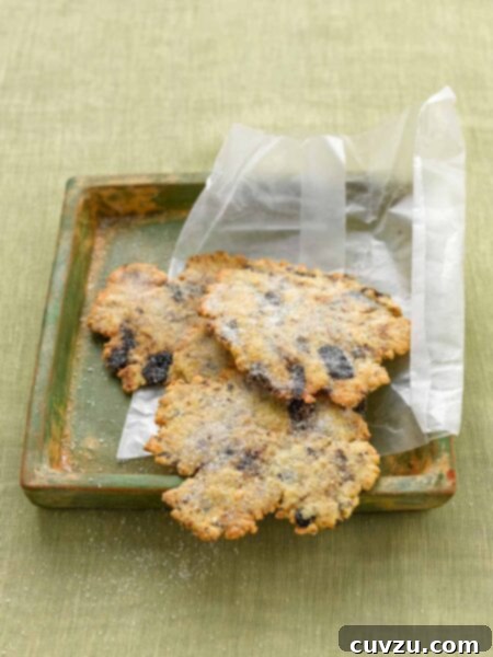 Irregular-shaped wafer cookies dotted with lemon and black olives in a wax paper wrapper on a green wood tray.