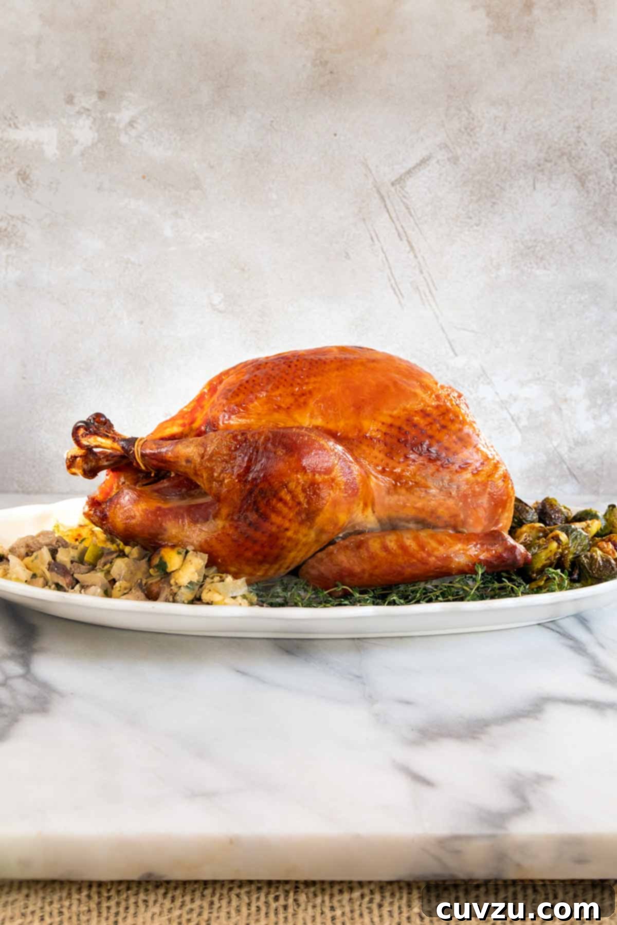 Flavorful Dry Brine Turkey 9 A cooked dry brined turkey on a bed of herbs with stuffing and roasted Brussels sprouts around it.