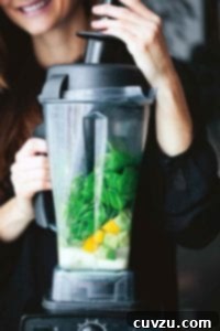 A woman with a Vitamix filled with spinach, mango, and milk, illustrating how to make a perfect smoothie.