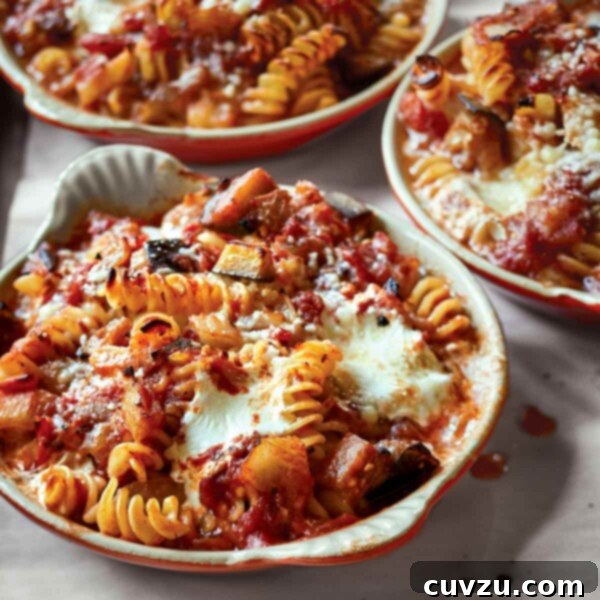 Close-up of baked pasta with tomatoes and eggplant, showing melted cheese and rich sauce.
