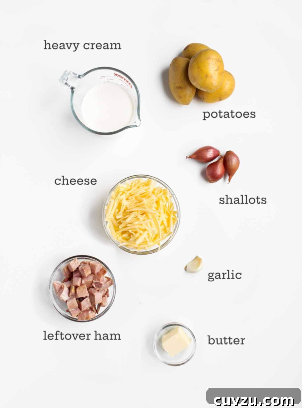 Comforting Ham & Potato Bake 3 A detailed arrangement of ingredients for a ham, cheese, and potato casserole, including heavy cream, neatly sliced Yukon Gold potatoes, aromatic shallots, garlic, a block of rich cheese, diced ham, and a knob of butter.