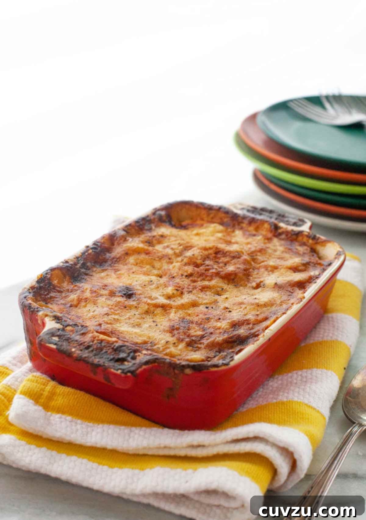 Comforting Ham & Potato Bake 4 A richly golden and bubbling ham, cheese, and potato casserole, served fresh from the oven in a large rectangular baking dish, resting on a red-and-white striped tea towel.