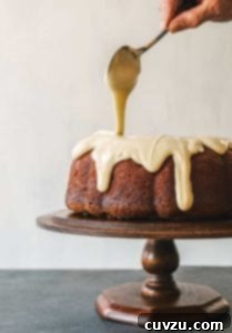 A Red Truck Bakery apple cake on a cake stand being drizzled with maple glaze.
