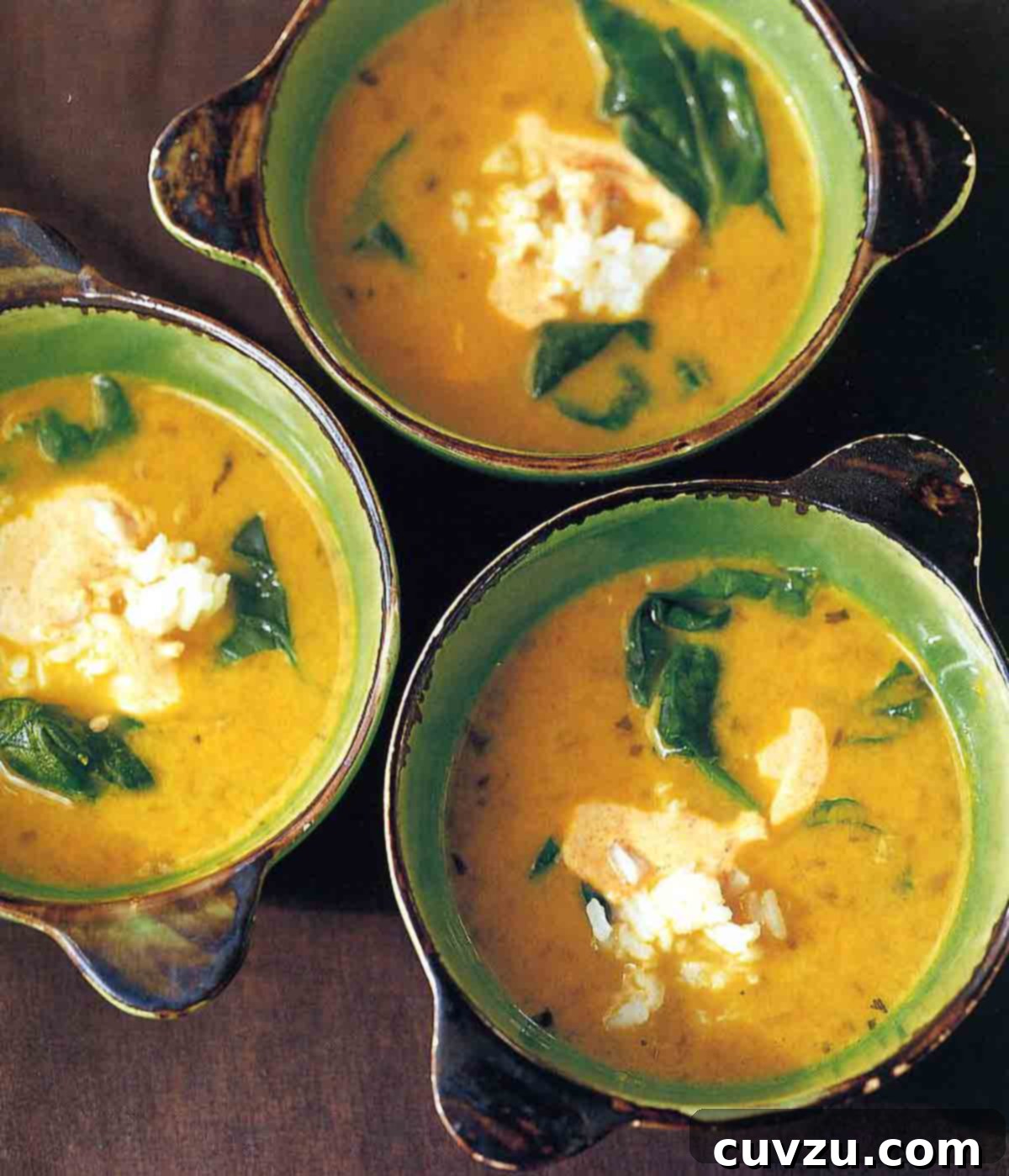 Tropical Golden Pea Coconut Soup 2 Three beautifully arranged bowls of creamy yellow pea and coconut milk soup, each garnished with fresh spinach leaves and a generous dollop of cooling yogurt, showcasing vibrant colors and enticing textures.