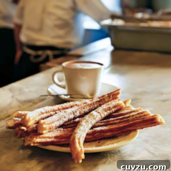 Crispy Golden Churros 3 A plate of churros with a cup of hot chocolate in the background