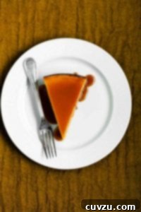 A slice of pure pumpkin cheesecake on a white plate drizzled with caramel glaze with a fork resting beside it.