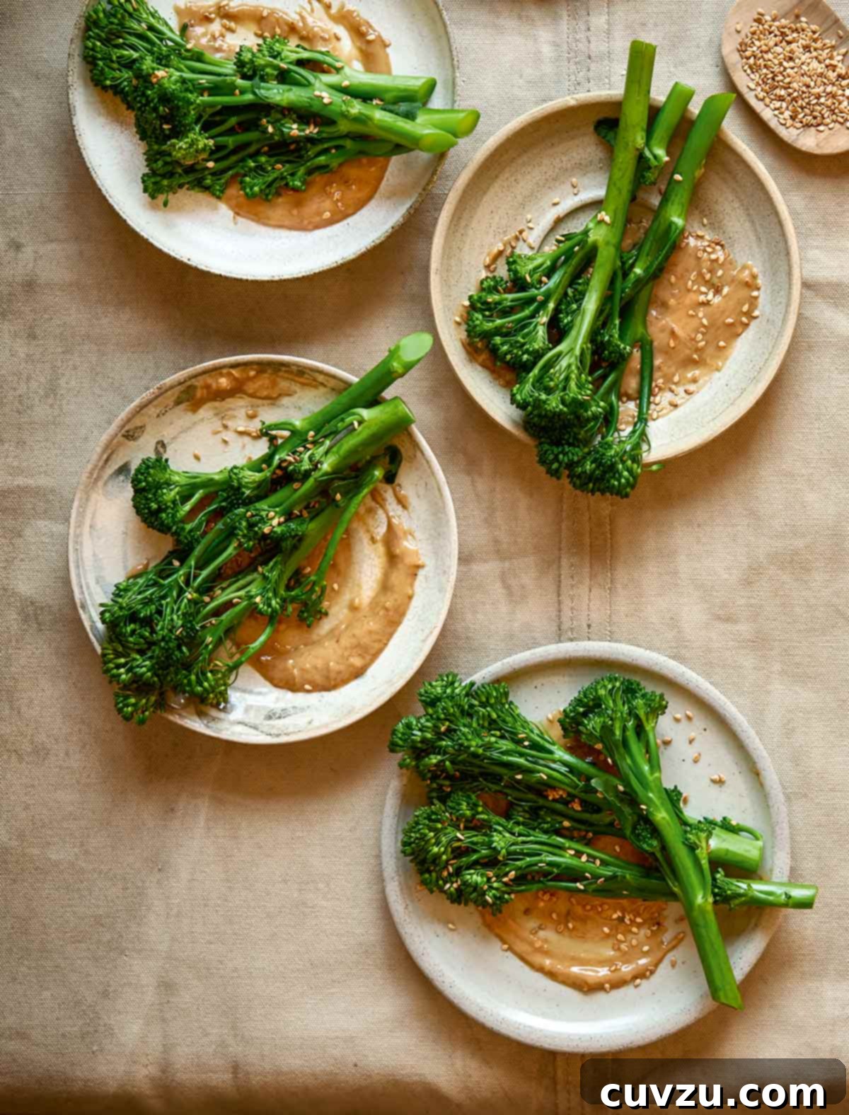 Peanut-Glazed Broccoli 2 Four plates topped with broccoli with peanut sauce and a small dish of sesame seeds on the side, garnished with fresh herbs.