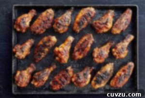 A rimmed baking sheet showcasing 18 grilled chicken wings coated in maple bourbon sauce.