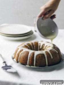 Grandma's Zucchini Cake 2 A beautifully glazed Old-Fashioned Zucchini Bundt Cake on a silver platter, with vibrant lemon glaze being drizzled over it, showcasing its moist texture and rich color.
