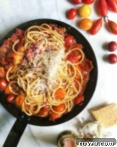 A black skillet filled with summer tomato pasta, sprinkled with fresh Parmesan cheese.