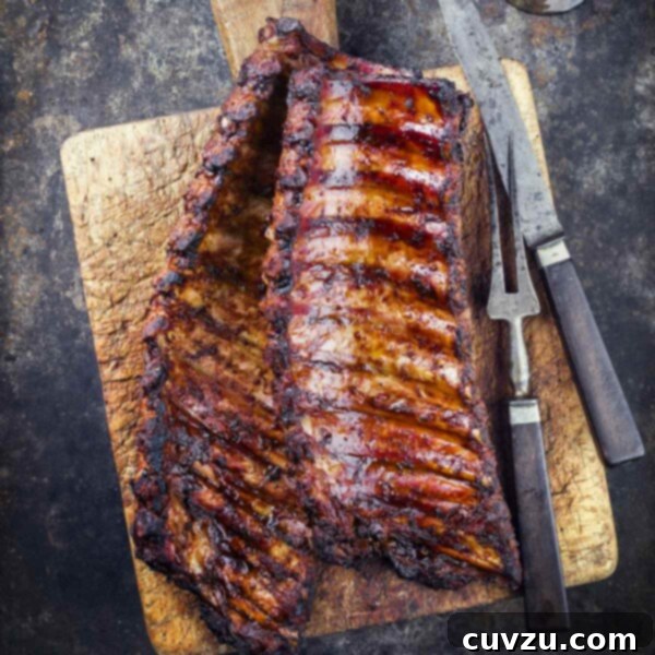 A wooden cutting board topped with two racks of smoked pork ribs, sliced and ready to serve, showing their tender interior.