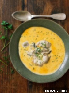 A ceramic bowl filled with oyster stew with several oysters in the center and a spoon resting beside the bowl.