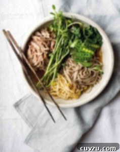 A bowl of chashu pork ramen, filled with braised pork, soba noodles, bean sprouts, peas, and bok choy, with a pair of chopsticks resting on top.