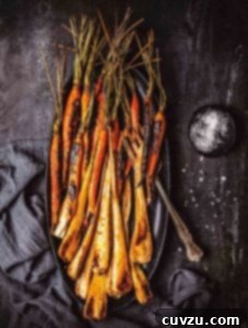 Maple glazed carrots with bourbon and parsnips on a black oval platter with a dish of salt beside it.