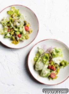 Two white plates of Italian restaurant salad made with iceberg, tomatoes, red onion, and Parmesan.