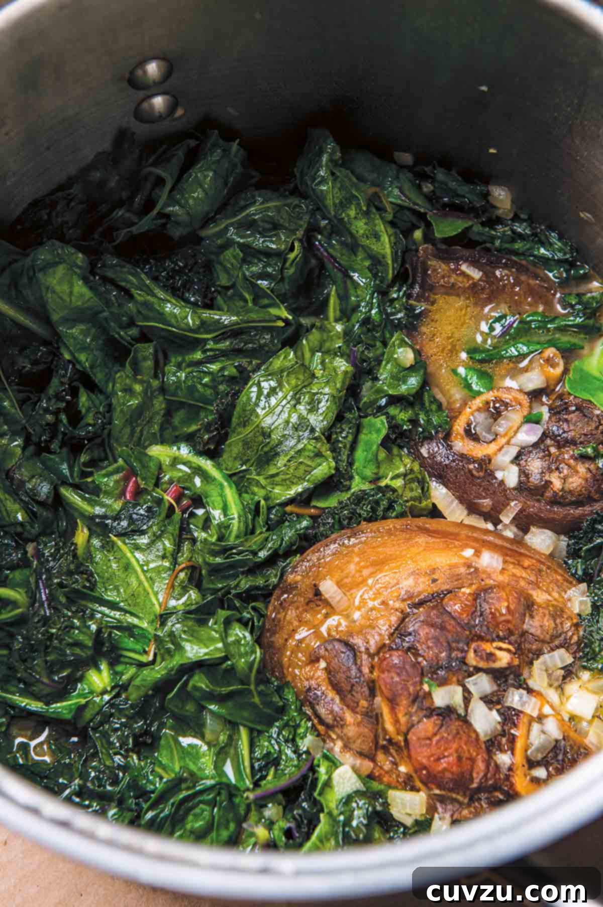 A large stock pot filled with tender Southern greens with ham hocks and chopped onions, ready to be served.