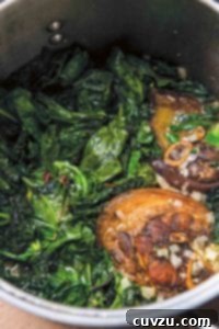 A large stock pot filled with Southern greens with ham hocks and chopped onions.