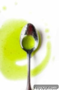 A silver spoon resting in a drizzle of basil oil on a white surface.