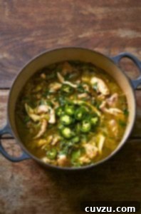 A large blue Dutch oven filled with green chicken chili, topped with sliced jalapenos.