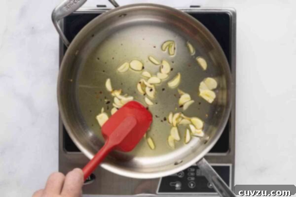 Blistered Skillet Broccolini 12 A person cooking garlic slices and pepper flakes in a skillet.