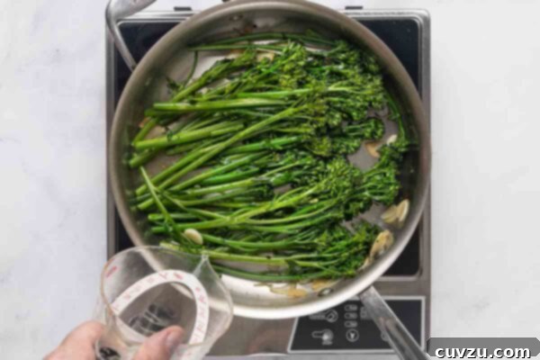 Blistered Skillet Broccolini 14 Broccolini and garlic in a skillet with a person pouring liquid into the skillet.