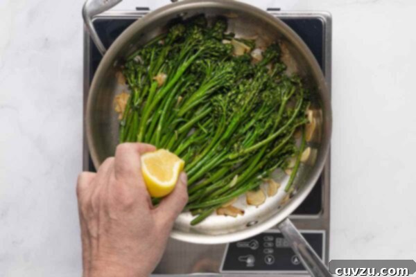 Blistered Skillet Broccolini 16 A person squeezing a lemon half into a skillet filled with broccolini and garlic.