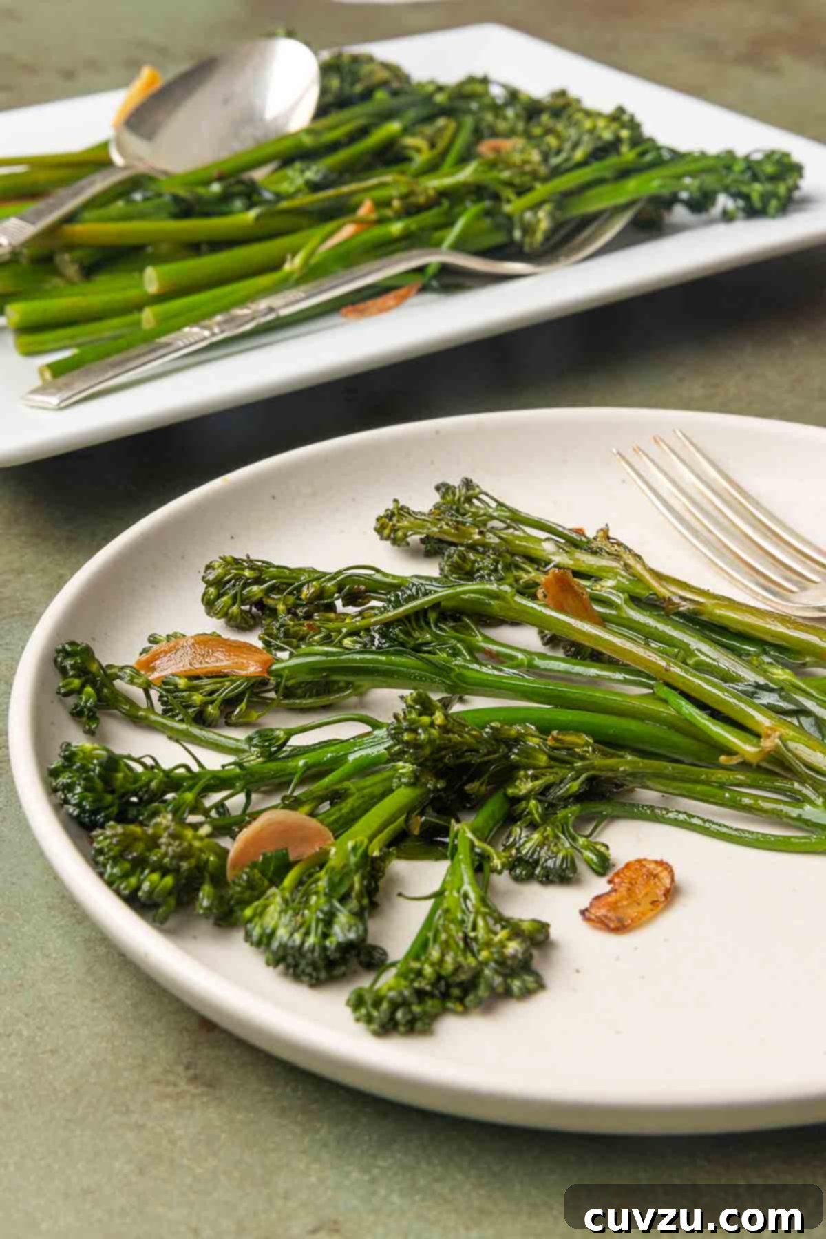 Blistered Skillet Broccolini 9 Seared broccolini and slices of browned garlic on a plate with a platter of broccolini in the background.