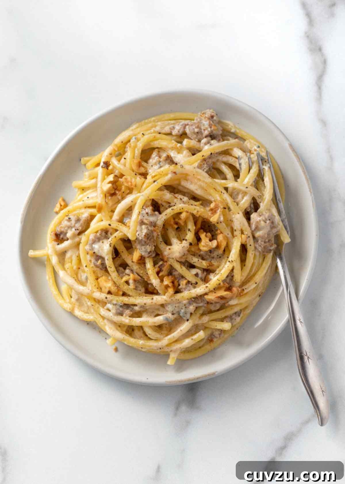 Robust Sausage & Blue Cheese Pasta with Toasted Walnuts 8 A white bowl filled with blue cheese, sausage, and walnut pasta with a fork resting on the side of the bowl.