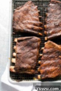 Four slabs of BBQ oven ribs on a rack inside a rimmed baking sheet.