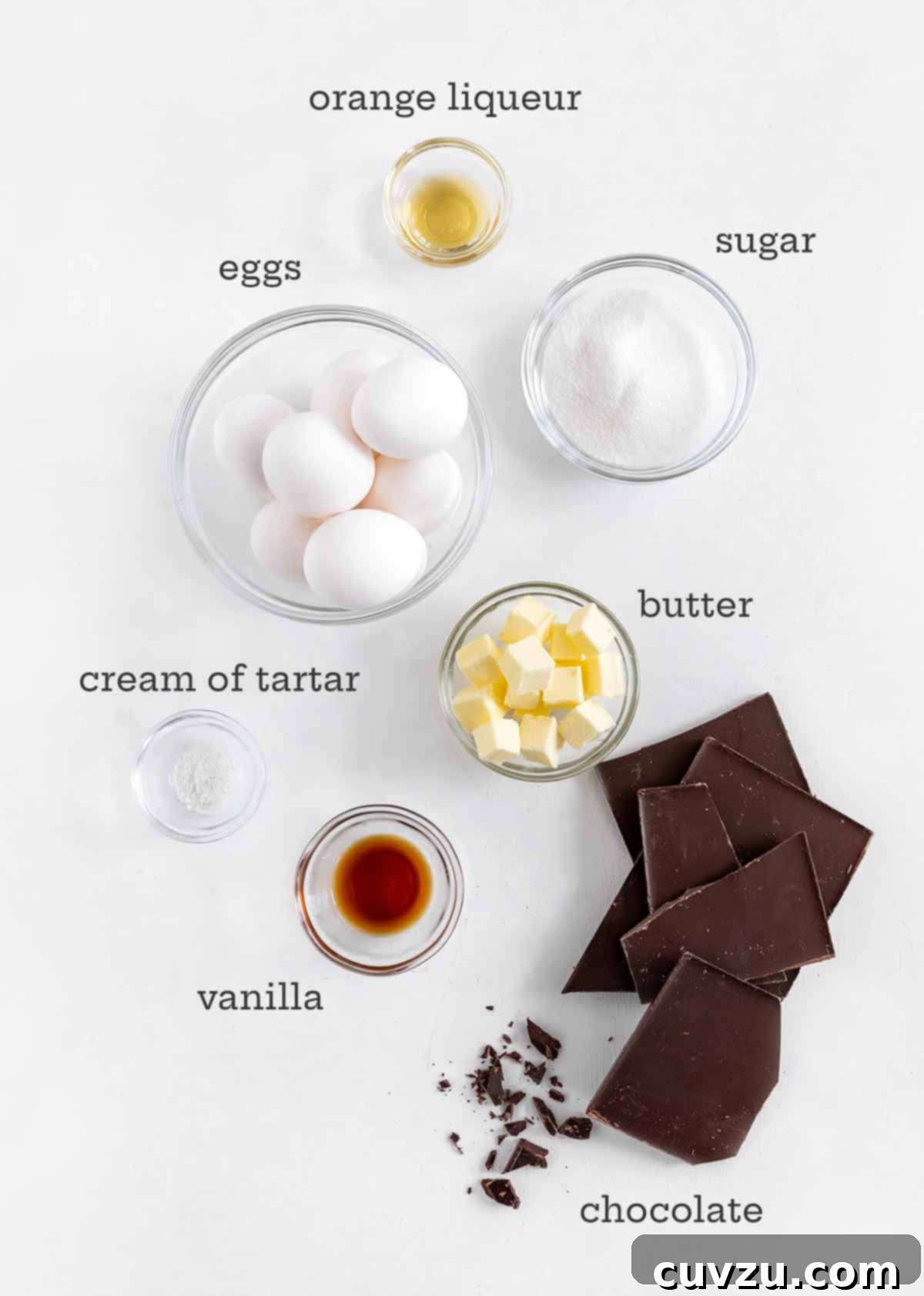 Decadent Chocolate Soufflé 4 Ingredients for a luscious chocolate soufflé: fresh eggs, dark chocolate, creamy butter, granulated sugar, aromatic vanilla extract, zesty orange liqueur, and a touch of cream of tartar, neatly arranged on a rustic surface.